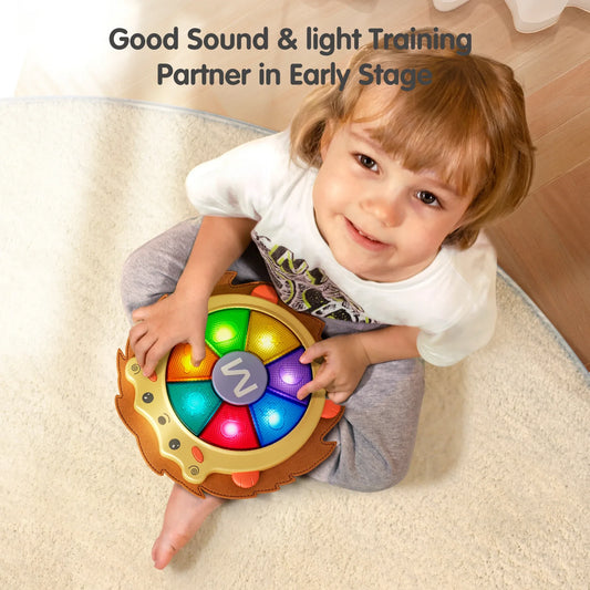 Smiling child sitting on a soft rug while playing with a hedgehog-shaped baby musical drum toy. The toy features glowing rainbow-colored light-up buttons in the center, providing sound and light interaction for early-stage training and entertainment.