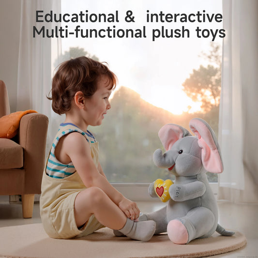 Smiling toddler playing on the floor with an interactive plush elephant toy holding a yellow heart, captioned 'Educational & interactive multi-functional plush toys'.