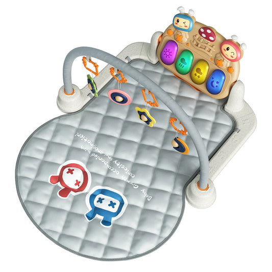 A baby play gym set featuring a quilted grey mat with two cartoon robot-like characters printed in red and blue. The gym has a sturdy white frame with two grey arches holding several colorful hanging toys, including star and ring rattles. At the top is a large interactive musical panel with glowing keys in purple, green, yellow, and blue, decorated with two cartoon bunny faces and a red mushroom design.