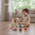 Young child sitting on the floor indoors, reaching toward a battery-operated toy dog as it walks and ‘barks,’ with its colorful accessories (rope ball, remote, toy bottle, bone in bowl) scattered around, overlaid with text ‘Walk and sing adding variety to playtime’ and musical notes.