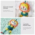 Yellow plush lion rattle with red‑and‑white gingham mane nestled in soft white stuffing; below it, the same lion toy floating in clear water to show it’s washable without fading.