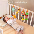 Baby lying in a crib reaching up to grab brightly colored animal plush rattles—elephant, giraffe, lion, and frog—suspended by orange elastic stretch rings from the crib rail.