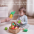 A hand holds a felted corn cob toy above a seated child’s head, who is grasping a green felted piece. Nearby, a basket overflows with assorted colorful felted vegetables on a light carpet.