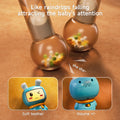 Close-up of the transparent ball at the bottom of a blue bunny-shaped musical rattle, showing colorful beads inside that make a soft rattling sound when shaken, like falling raindrops. Two smaller inset images highlight the soft teether bunny ears and the volume control on the back of the toy.