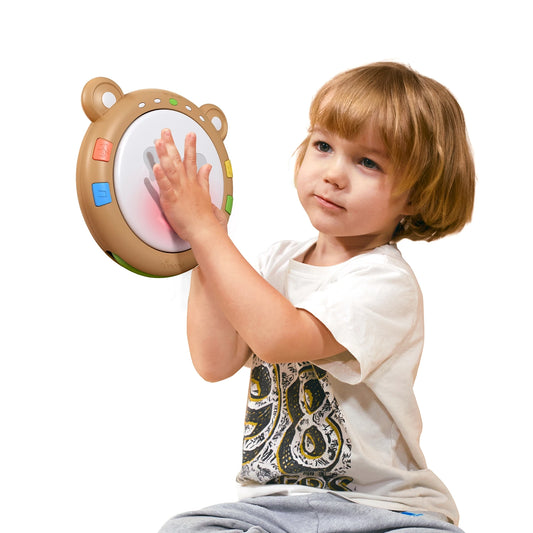 A toddler plays with a light-up baby drum toy designed for early musical education. The round drum features a bear-ear design, colorful buttons around the edge, and a large illuminated surface that lights up red when tapped. Ideal for babies and toddlers to explore rhythm, sound, and sensory development.