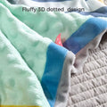 Close-up of a baby security blanket with a fluffy 3D dotted texture in soft mint green fabric, bordered with blue, yellow, and gray edges. A small pink polka-dot tag is visible for tactile play. Text above reads: “Fluffy 3D dotted design.”