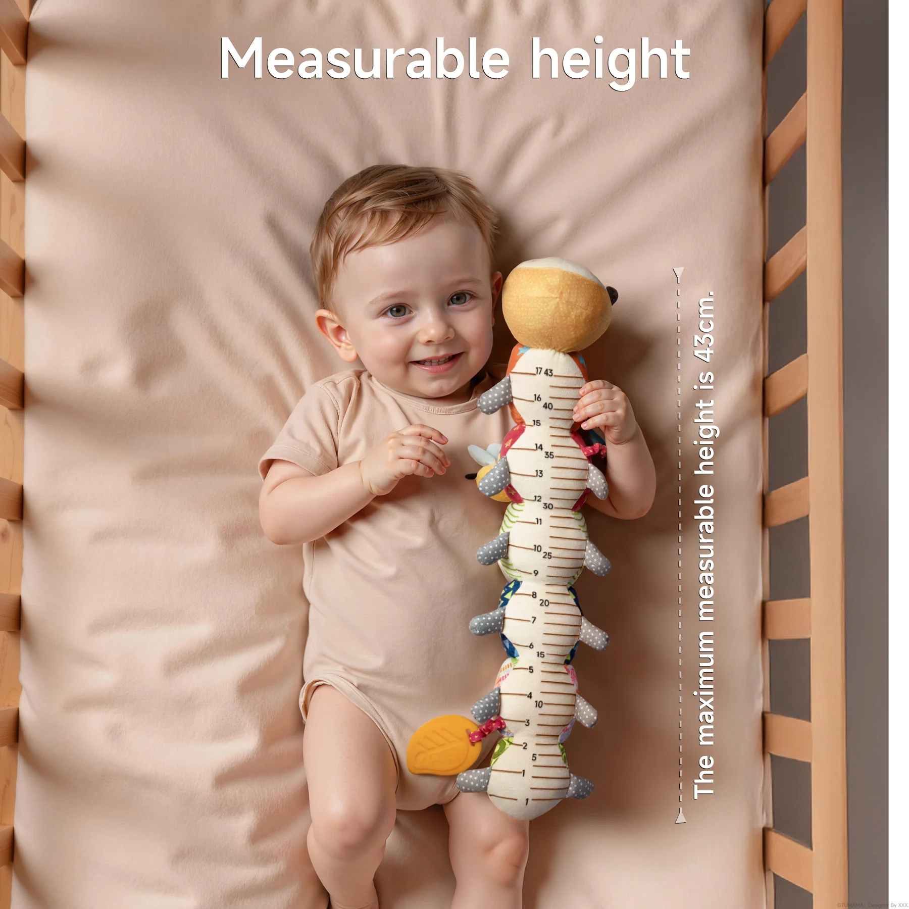 Smiling baby lying in a crib holding a plush caterpillar toy with a built-in height measurement scale; text overlay indicates the maximum measurable height is 43 cm.